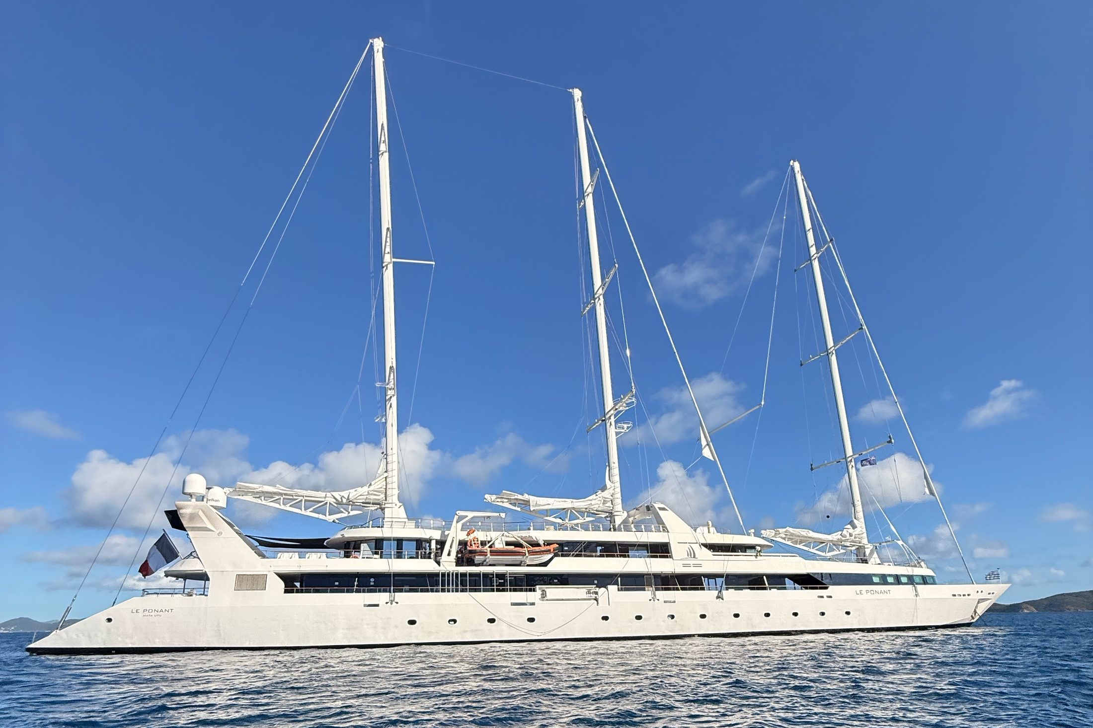 Le Ponant at anchor, three masts against a blue sky, seen from the tender